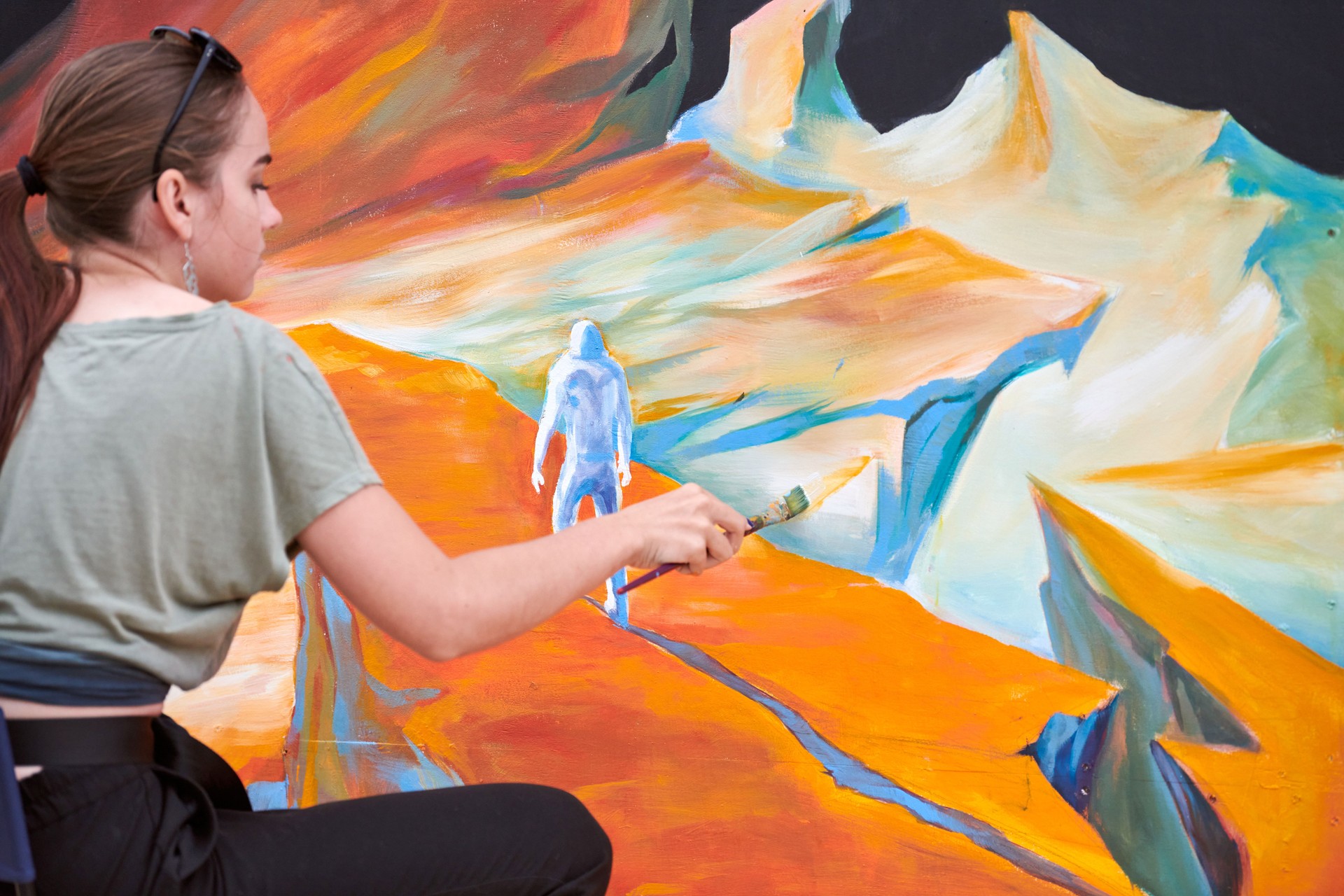 Attractive female painter passionately draws picture with paintbrush sitting on chair for exhibition